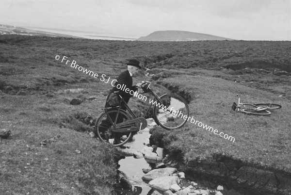 MAN CROSSING STREAM CARRYING BICYCLE